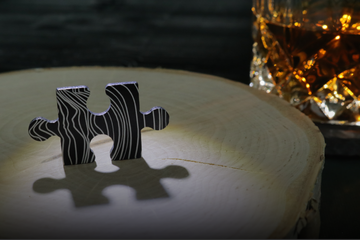 Metal puzzle piece standing beside a whiskey glass