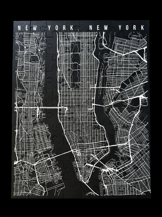 A black and white New York City street map jigsaw puzzle, fully assembled and framed by a black background, with 'NEW YORK, NEW YORK' written across the top.
